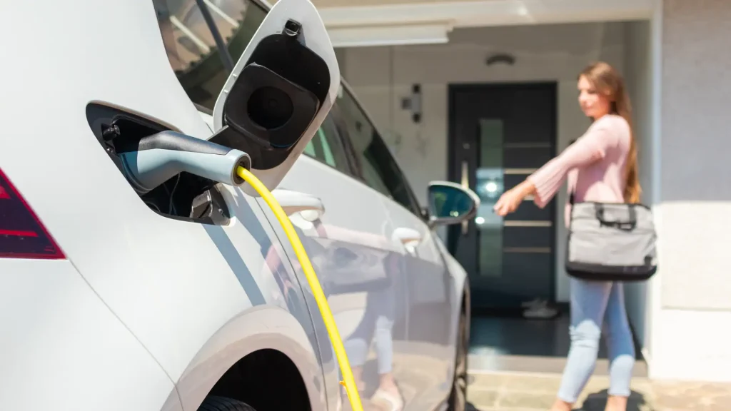 Woman charging her electric vehicle from a home EV charger installed near the front porch of her Miami residence.