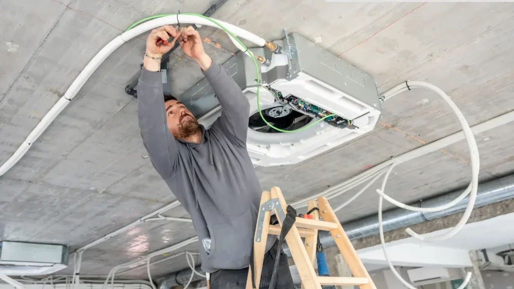 ceiling fan Technician performing ceiling-mounted equipment replacement and electrical wiring in a commercial space.